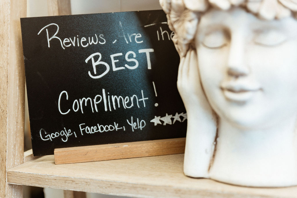 Chalkboard sign in the salon reading: Reviews are the best compliment — Google, Facebook, Yelp